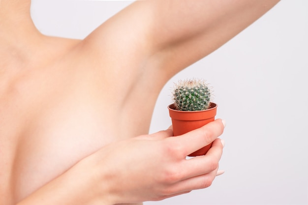 Mujer joven que sostiene el cactus verde cerca de la axila.