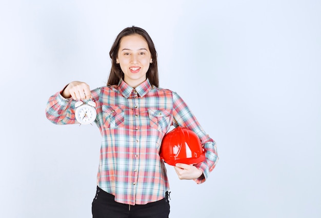 Una mujer joven que sostiene un casco y un reloj de alarma.