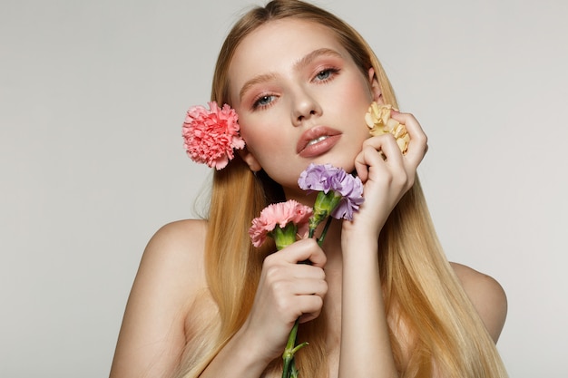 Mujer joven que sostiene las flores y que presenta en un estudio