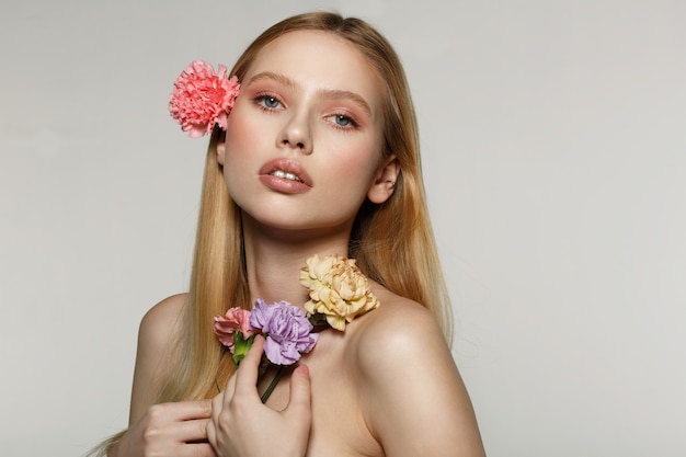 Mujer joven que sostiene las flores y que presenta en un estudio