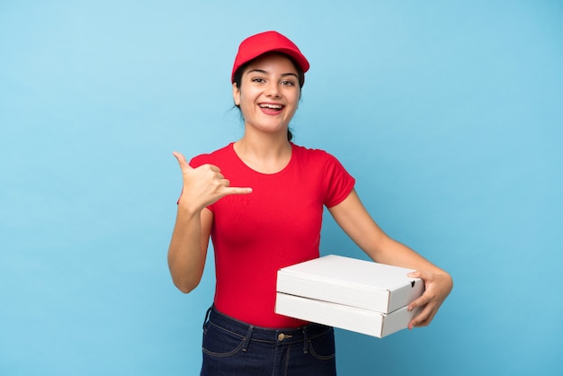 Mujer joven que sostiene una pizza sobre la pared rosada aislada que hace gesto del teléfono