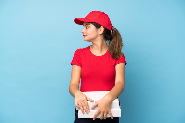 Foto mujer joven que sostiene una pizza sobre la pared rosada aislada que mira al lado