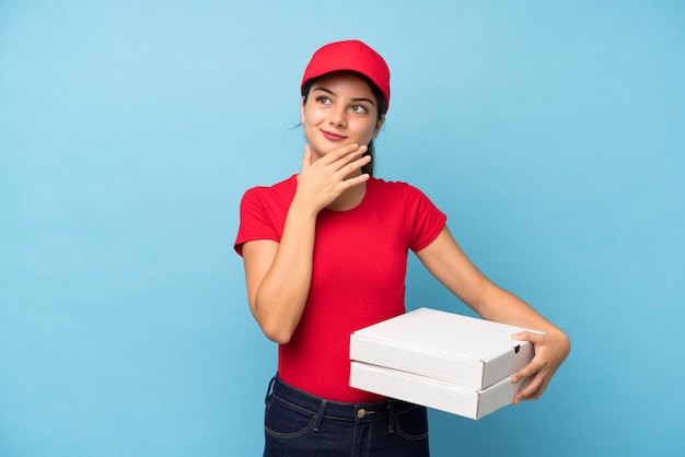 Mujer joven que sostiene una pizza sobre la pared rosada aislada que piensa una idea