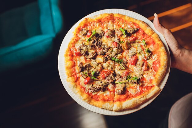 Mujer joven que sostiene la placa con la pizza sabrosa, visión ascendente cercana.