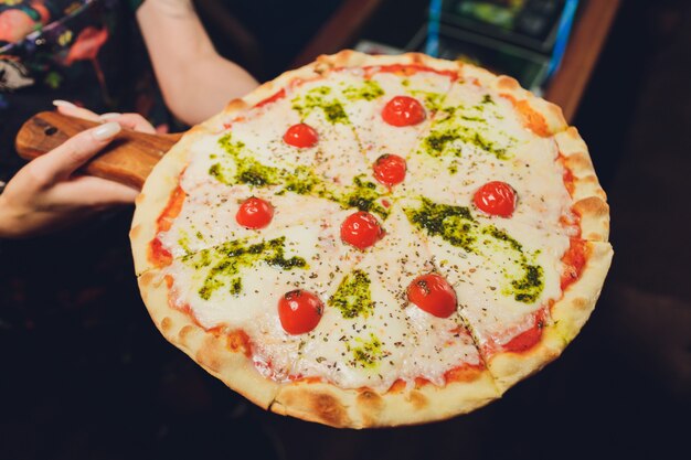 Mujer joven que sostiene la placa con la pizza sabrosa, visión ascendente cercana.