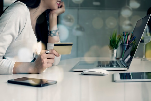 Mujer joven que sostiene la tarjeta de crédito y que usa el ordenador portátil. Concepto de compras en línea