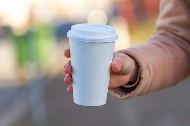 Mujer joven que sostiene la taza de café de papel en un día soleado