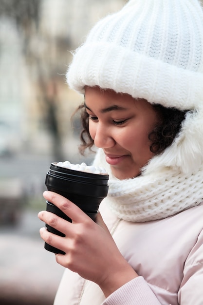 Mujer joven que sostiene la taza de café reutilizable en el invierno