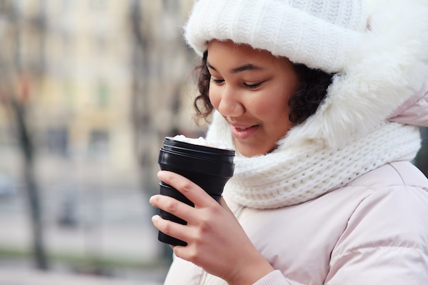 Mujer joven que sostiene la taza de café reutilizable en el invierno