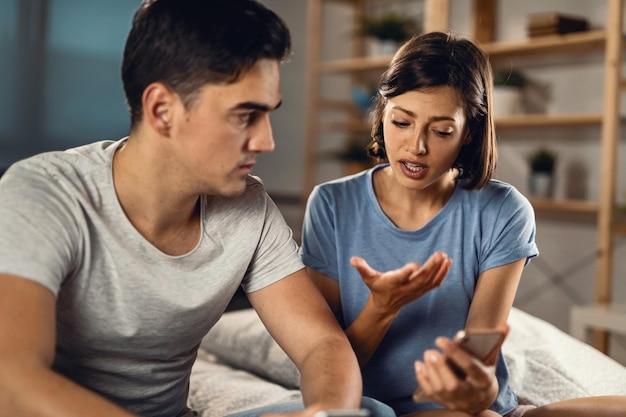 Mujer joven que tiene un conflicto con su novio y discute sobre mensajes de texto en el teléfono móvil en casa