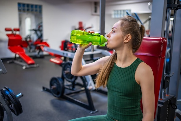Mujer joven que tiene un descanso después del entrenamiento deportivo y bebe agua de una botella de vidrio verde Equilibrio de vida de autocuidado y concepto de estilo de vida saludable