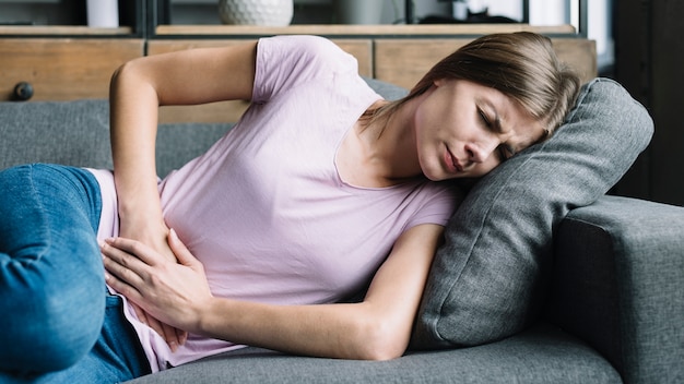 Foto mujer joven que tiene dolor de estómago que miente en el sofá
