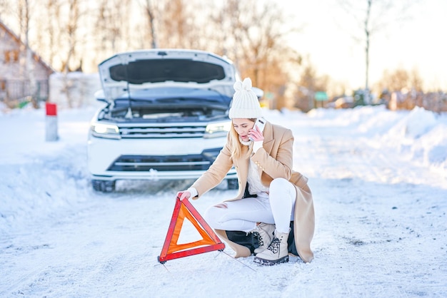 Mujer joven que tiene problemas con el coche en invierno. Foto de alta calidad