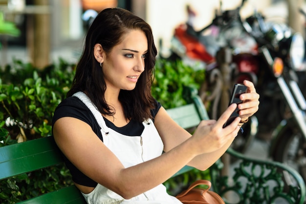 Mujer joven que toma las fotografías con su teléfono elegante al aire libre.