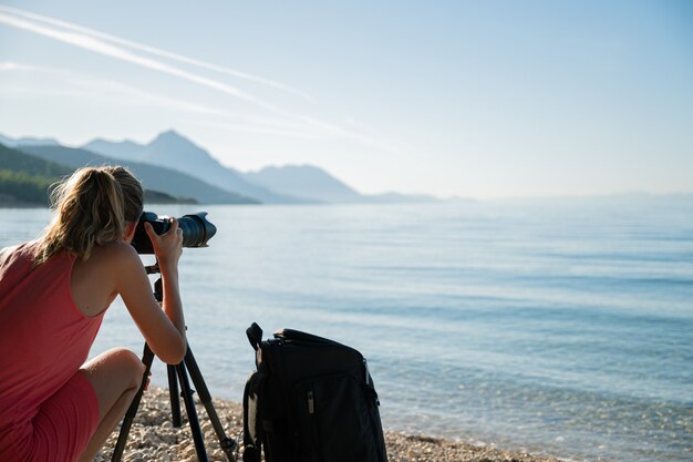 Mujer joven que toma fotos del mar hermoso de la mañana