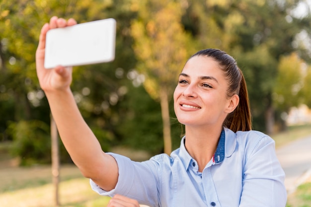 Mujer joven que toma el selfie en banco en el parque