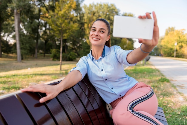 Mujer joven que toma el selfie en banco en el parque