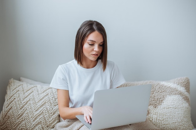 Mujer joven que trabaja en la computadora portátil en casa en la cama