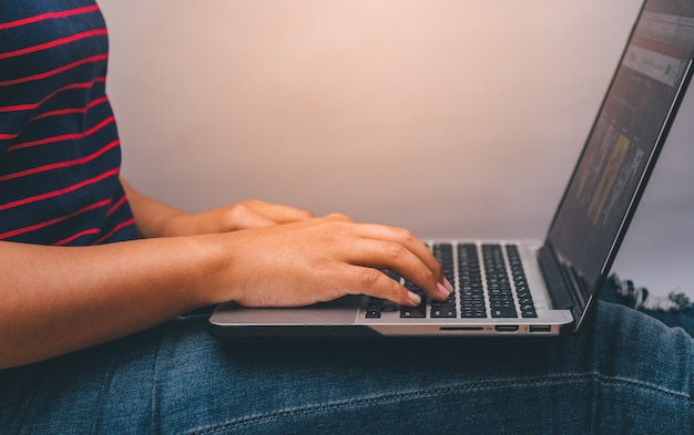 Mujer joven que trabaja en la computadora portátil mientras está sentado en el piso de madera con luz solar