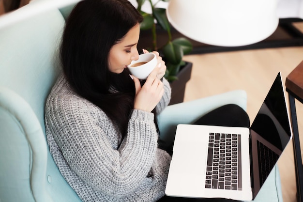 Mujer joven que trabaja en la computadora portátil mientras está sentado en la sala de estar.