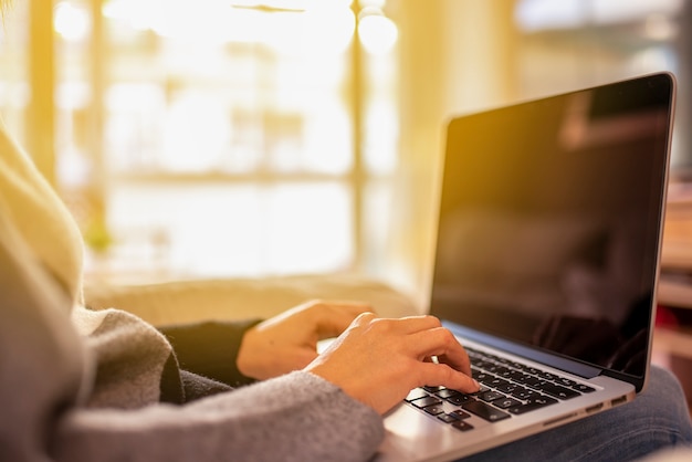 Mujer joven que trabaja en la computadora portátil sentado en casa al atardecer