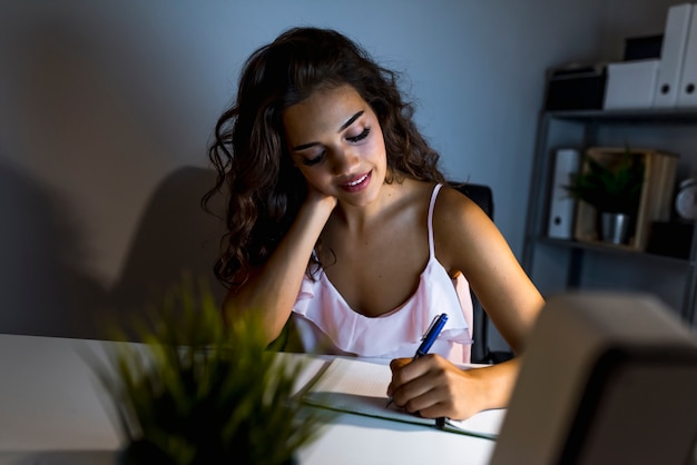 Mujer joven que trabaja y estudia a altas horas de la noche, se conecta con su computadora y wr