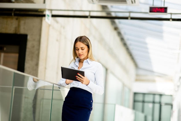 Mujer joven que trabaja en una tableta digital en el pasillo de la oficina