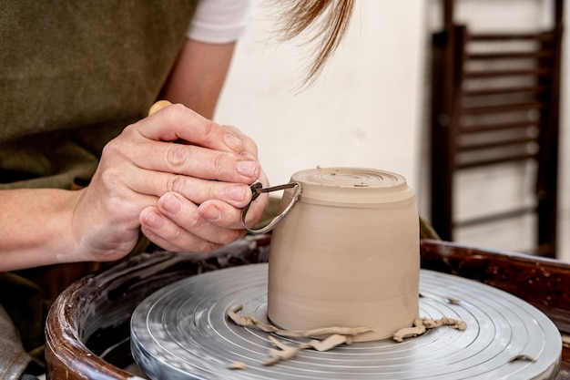 Mujer joven que trabaja en el torno de alfarero Mujer joven ceramista haciendo productos de arcilla en torno de cerámica en el estudio Primer plano de manos femeninas trabajando en el torno de alfarero