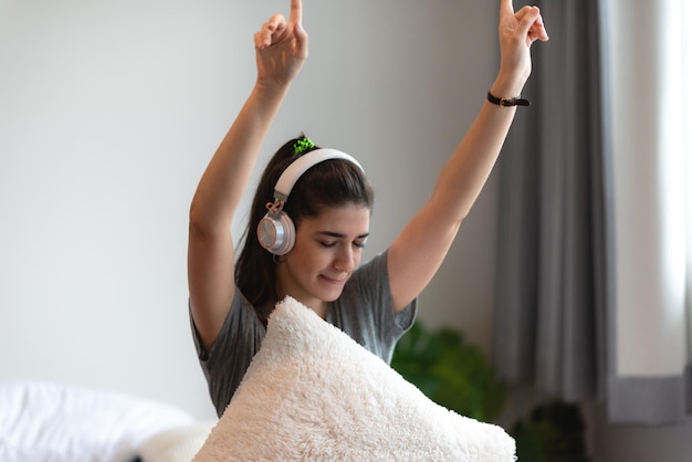 Mujer joven que usa auriculares o audífonos para relajarse con una canción en la cama en el dormitorio en casa concepto de sonido feliz escuchar estilo de vida en una sensación de audio acogedora