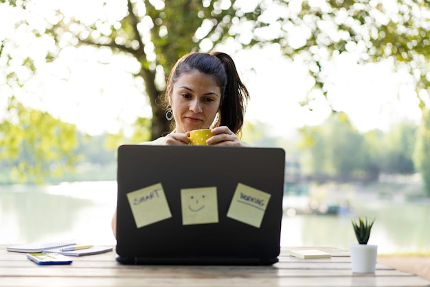 Mujer joven que usa una computadora portátil en el parque público Mujer independiente milenaria que trabaja de forma remota detrás de una computadora portátil de primer plano en un parque de la ciudad Concepto de tecnología y trabajo remoto Uso de dispositivos tecnológicos