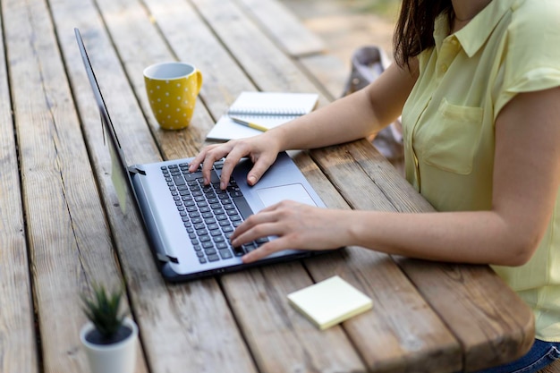 Mujer joven que usa una computadora portátil en el parque público Mujer independiente milenaria que trabaja de forma remota detrás de una computadora portátil de primer plano en un parque de la ciudad Concepto de tecnología y trabajo remoto Uso de dispositivos tecnológicos