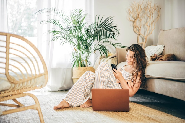 Mujer joven que usa la computadora portátil en el sofá en casa