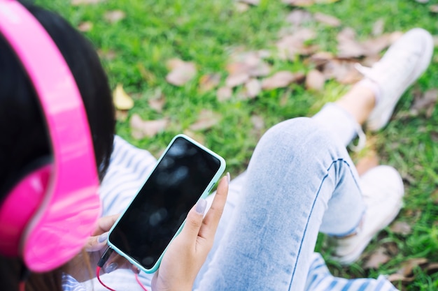 La mujer joven que usa música móvil y que escucha con los auriculares en jardín con relaja