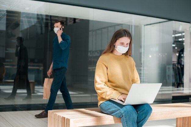 Mujer joven que usa su computadora portátil en la calle durante la cuarentena. concepto de protección de la salud