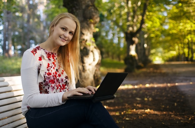 Mujer joven que usa su computadora portátil en el parque