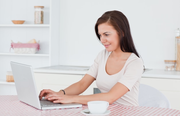 Mujer joven que usa su computadora portátil y que tiene un té