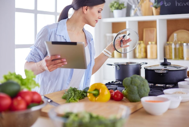 Mujer joven que usa una tableta para cocinar en su cocina