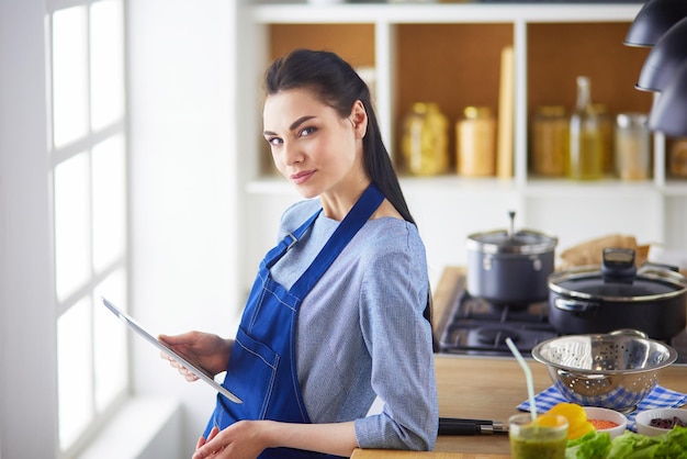 Mujer joven que usa una tableta para cocinar en su cocina