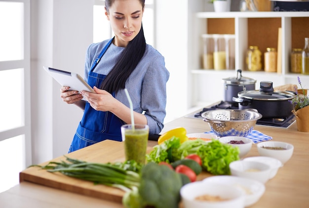 Mujer joven que usa una tableta para cocinar en su cocina