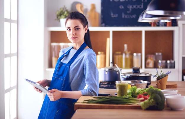 Mujer joven que usa una tableta para cocinar en su cocina