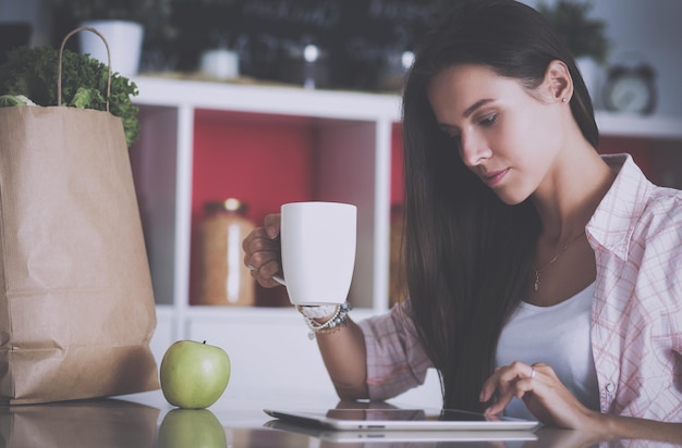 Mujer joven que usa una tableta para cocinar en su cocina