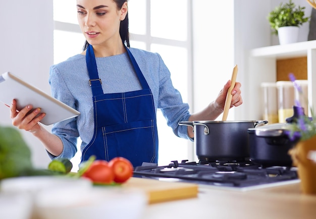 Mujer joven que usa una tableta para cocinar en su cocina