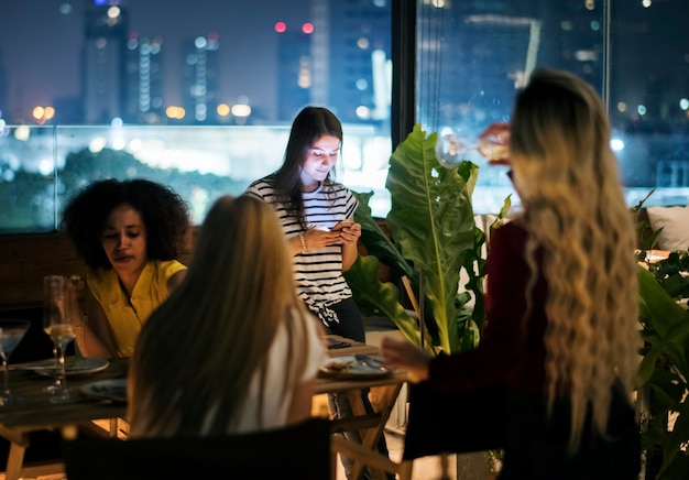 Foto mujer joven que usa un teléfono inteligente en una noche de cena sin interacción con amigos