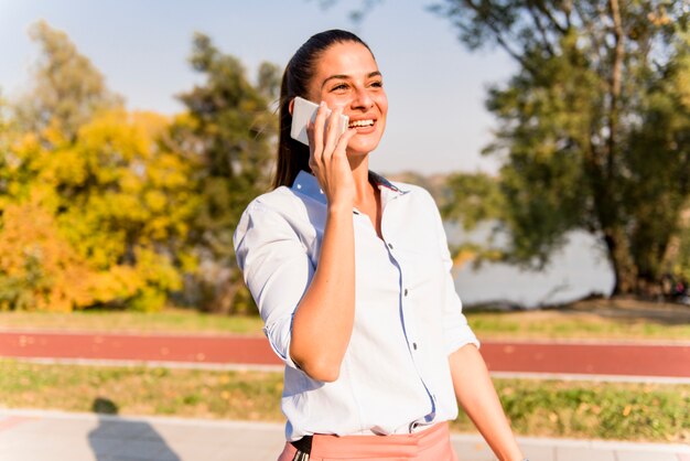 Mujer joven que usa el teléfono móvil en el parque por el río