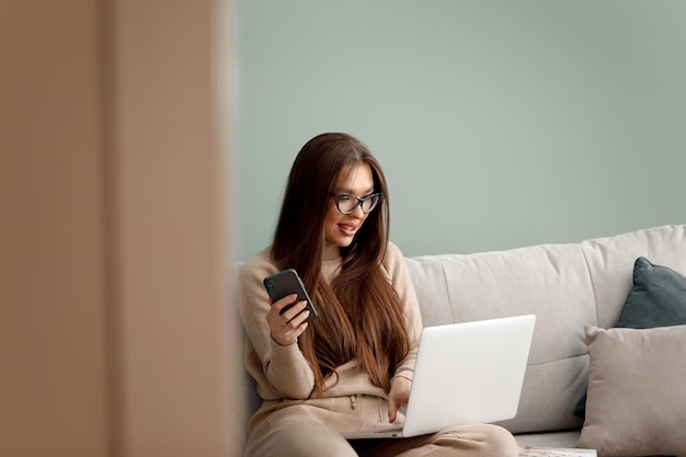 Mujer joven que usa el teléfono y trabaja en la computadora portátil en casa hermosa chica de compras