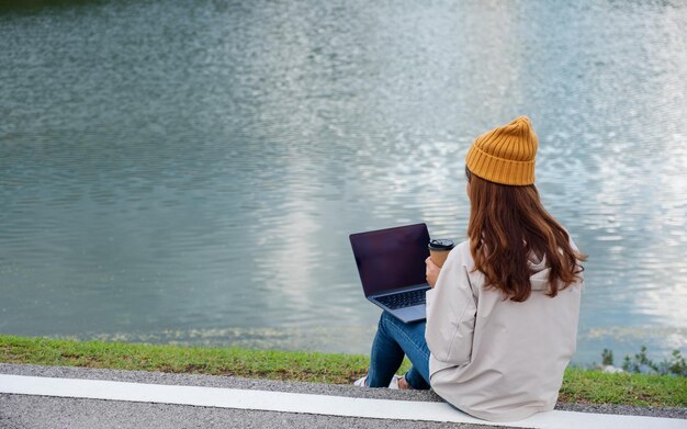 Una mujer joven que usa y trabaja en una computadora portátil mientras viaja por las montañas y el lago