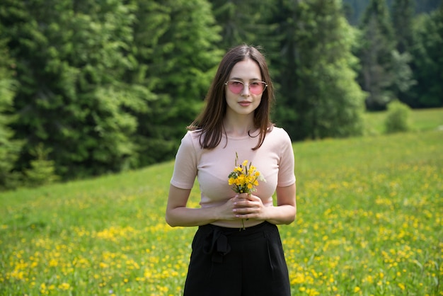 Mujer joven con ramo de flores silvestres en un césped soleado.