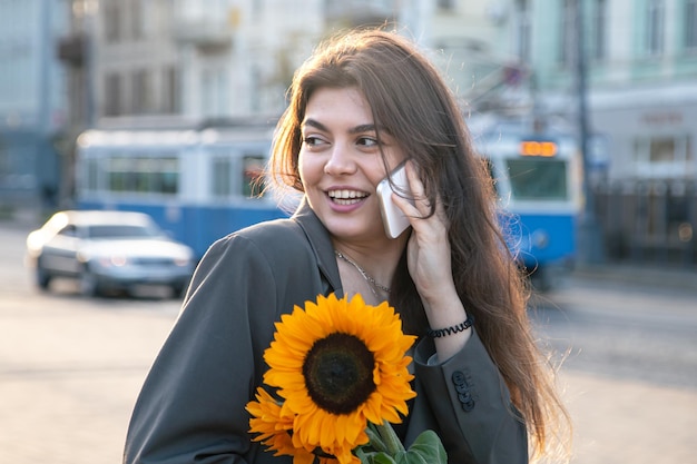 Una mujer joven con un ramo de girasoles está hablando por teléfono al atardecer