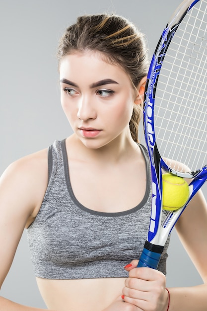 Mujer joven con una raqueta de tenis sobre su cara aislada. Rostro neutral y mirada segura. Fotografía de cerca.