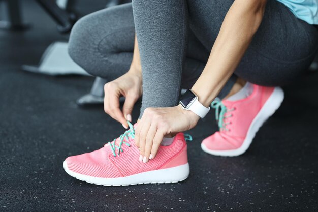 Mujer joven con rastreador de fitness atarse los cordones de los zapatos en el primer plano del gimnasio